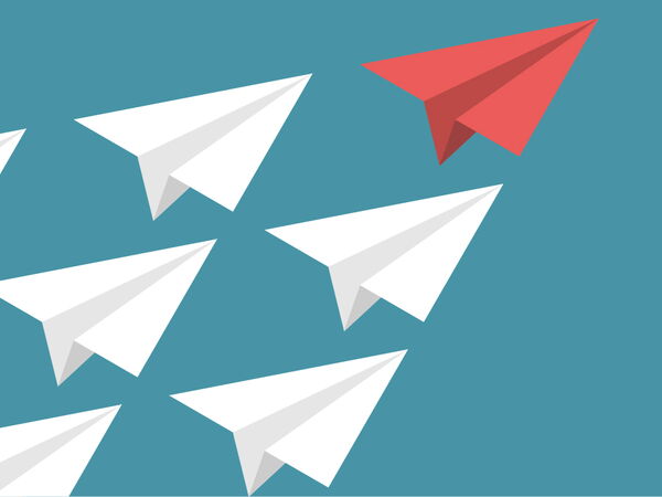 weiße Papierflieger folgen rotem Papierflieger als Symbolbild für das Thema „Führungskompetenz - Stärken stärken”