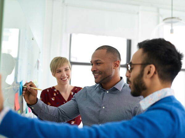 Team von Kolleg:innen vor dem Whiteboard in einem kreativen Meeting