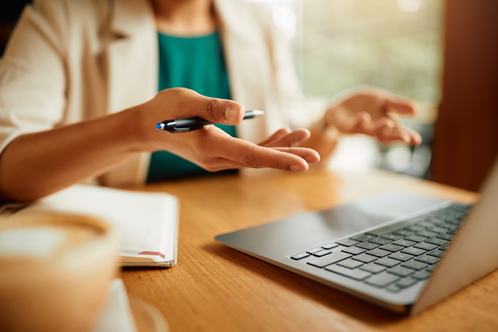 gestikulierende Frauenhände am Tisch vor einem aufgeklappten Laptop